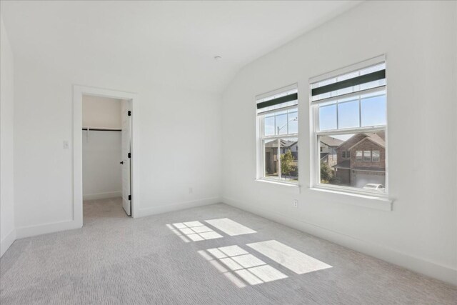 unfurnished bedroom featuring lofted ceiling, light colored carpet, a spacious closet, and a closet