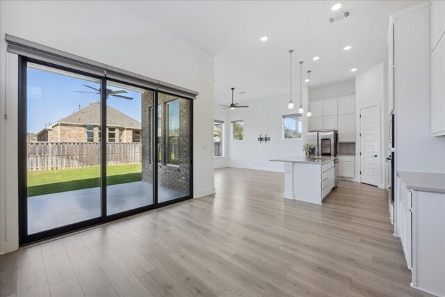 kitchen with a center island with sink, stainless steel fridge, light wood-type flooring, decorative light fixtures, and white cabinetry