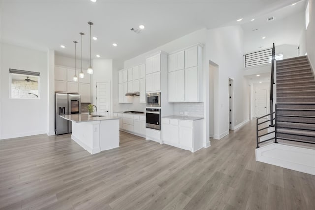 kitchen with white cabinetry, a center island with sink, light hardwood / wood-style flooring, and appliances with stainless steel finishes