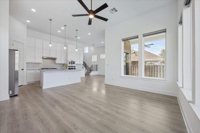 kitchen with appliances with stainless steel finishes, decorative light fixtures, white cabinets, backsplash, and a center island with sink