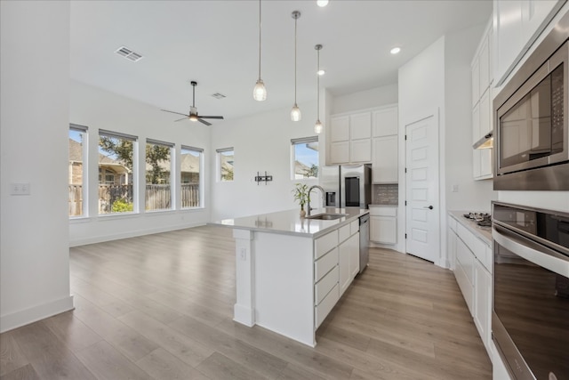 kitchen with white cabinets, sink, light hardwood / wood-style flooring, an island with sink, and appliances with stainless steel finishes