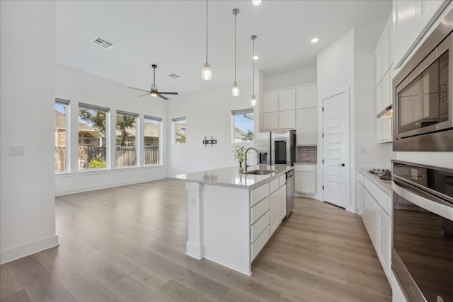 kitchen with pendant lighting, sink, stainless steel appliances, white cabinets, and a center island with sink