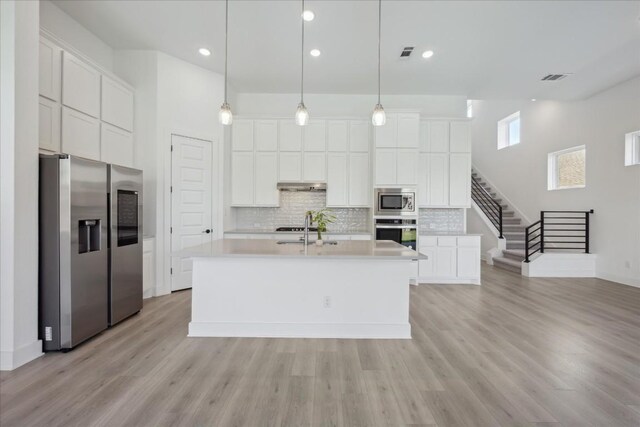 kitchen with appliances with stainless steel finishes, light hardwood / wood-style floors, white cabinetry, and an island with sink