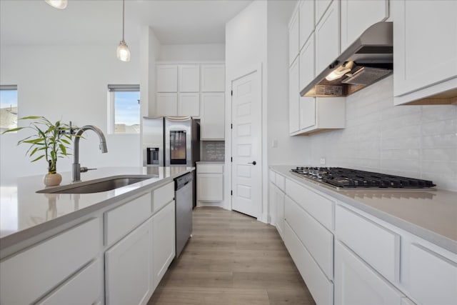 kitchen featuring appliances with stainless steel finishes, ventilation hood, pendant lighting, light hardwood / wood-style flooring, and white cabinets