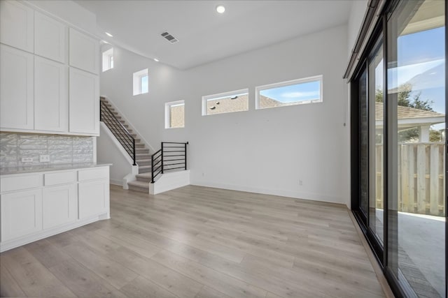 unfurnished living room with light wood-type flooring and a towering ceiling