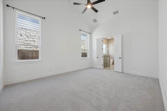 unfurnished bedroom with connected bathroom, multiple windows, ceiling fan, and high vaulted ceiling