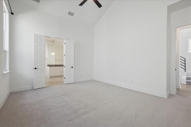 unfurnished bedroom with light carpet, ensuite bath, high vaulted ceiling, and ceiling fan