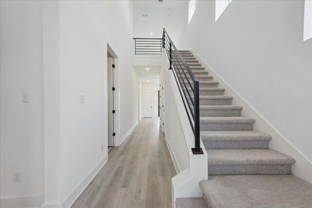 stairway with wood-type flooring and a towering ceiling