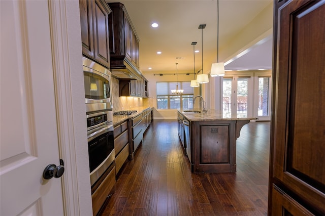 kitchen with appliances with stainless steel finishes, a kitchen bar, a spacious island, dark hardwood / wood-style flooring, and light stone counters