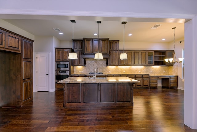 kitchen featuring decorative backsplash, dark hardwood / wood-style flooring, an island with sink, light stone countertops, and pendant lighting