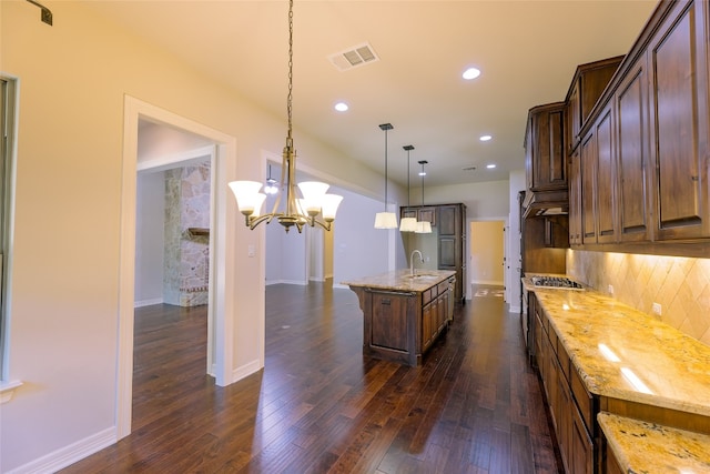 kitchen with light stone countertops, dark hardwood / wood-style floors, a kitchen island with sink, and hanging light fixtures