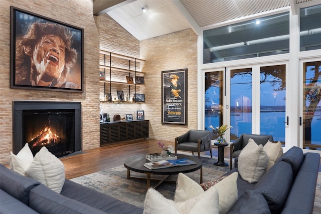 living room with beamed ceiling, wood-type flooring, a large fireplace, brick wall, and high vaulted ceiling