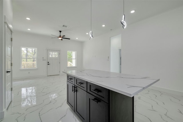 kitchen featuring ceiling fan, a center island, decorative light fixtures, and light stone countertops