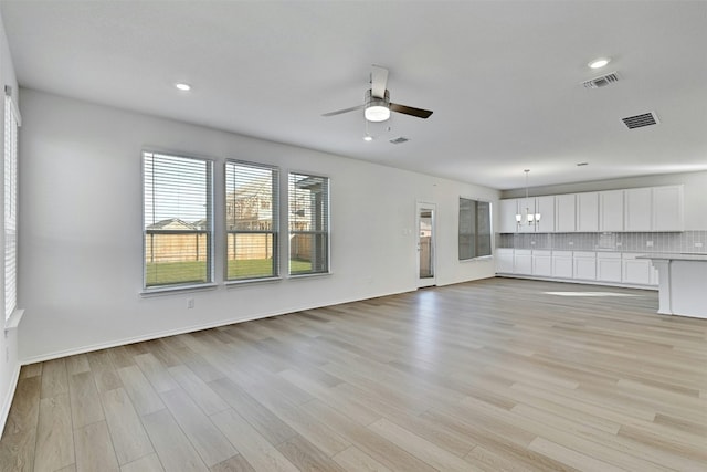 unfurnished living room featuring ceiling fan with notable chandelier and light hardwood / wood-style floors