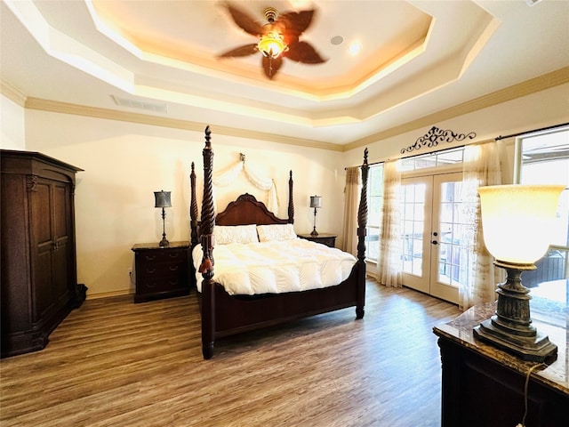 bedroom featuring wood-type flooring, ceiling fan, french doors, access to outside, and a tray ceiling