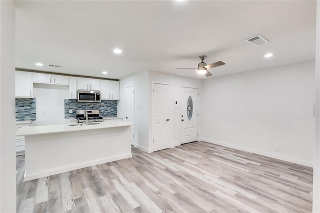 kitchen with light wood-type flooring, ceiling fan, stainless steel appliances, white cabinets, and decorative backsplash