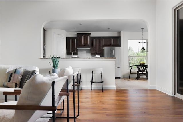 kitchen featuring stainless steel fridge, light hardwood / wood-style floors, dark brown cabinetry, light stone counters, and a notable chandelier