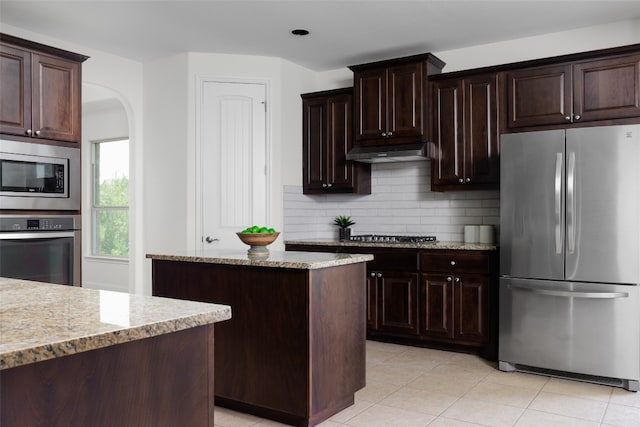 kitchen with light stone countertops, tasteful backsplash, appliances with stainless steel finishes, and dark brown cabinets