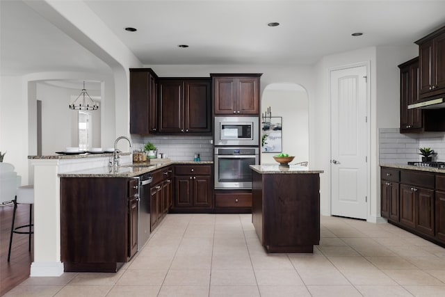 kitchen featuring light stone countertops, appliances with stainless steel finishes, sink, kitchen peninsula, and pendant lighting