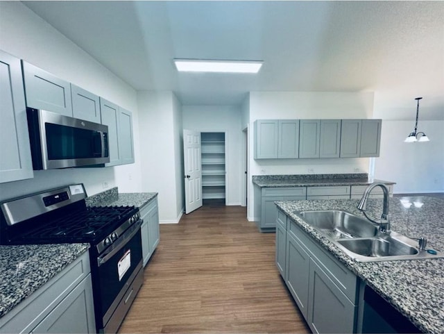 kitchen featuring sink, stainless steel appliances, dark stone counters, pendant lighting, and wood-type flooring