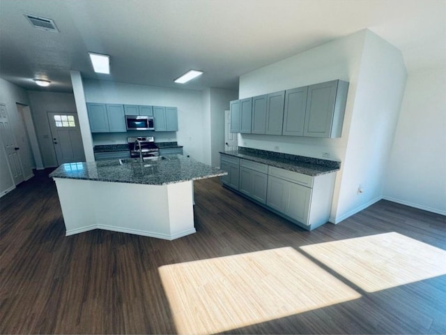 kitchen with gray cabinetry, stainless steel appliances, a kitchen island with sink, and dark wood-type flooring