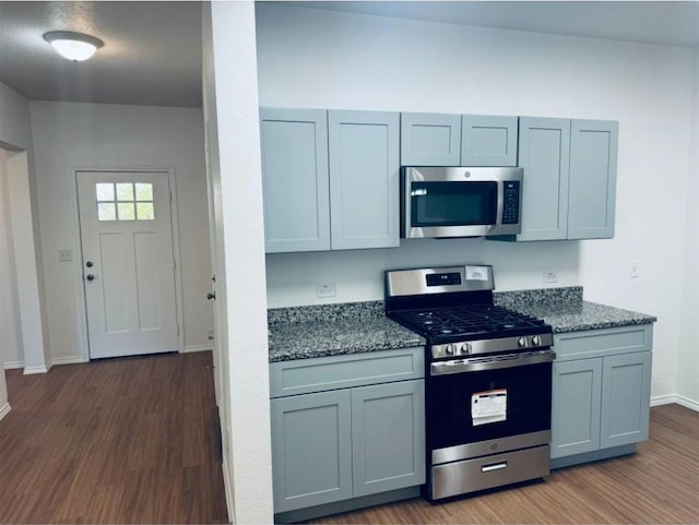 kitchen featuring gray cabinets, stainless steel appliances, dark stone counters, and dark wood-type flooring