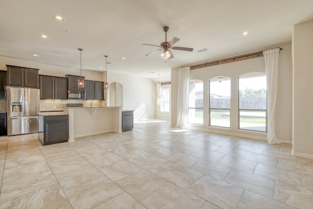 kitchen with tasteful backsplash, ceiling fan, decorative light fixtures, stainless steel fridge with ice dispenser, and a kitchen island with sink