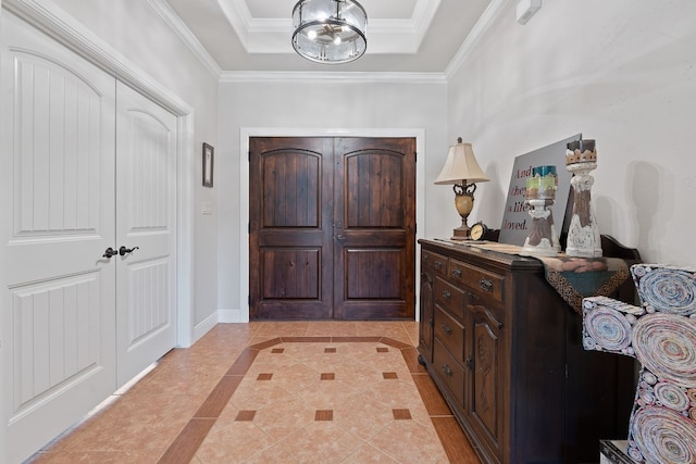 tiled foyer with ornamental molding, a tray ceiling, and an inviting chandelier