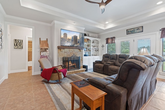 living room featuring a stone fireplace, ornamental molding, a raised ceiling, and light tile patterned floors