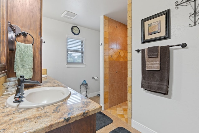 bathroom with a tile shower, vanity, and tile patterned floors