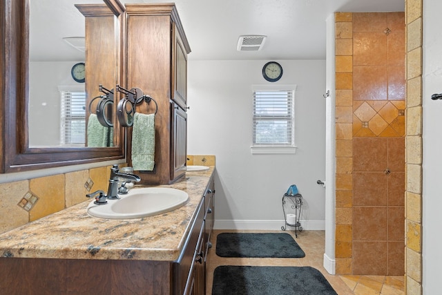 bathroom with vanity, decorative backsplash, a tile shower, and plenty of natural light