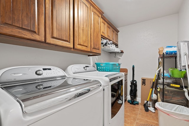 clothes washing area with cabinets, washing machine and clothes dryer, and light tile patterned floors