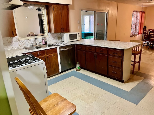 kitchen with kitchen peninsula, backsplash, a kitchen breakfast bar, sink, and white appliances