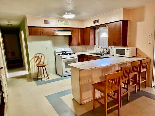 kitchen with sink, a breakfast bar, kitchen peninsula, and white appliances