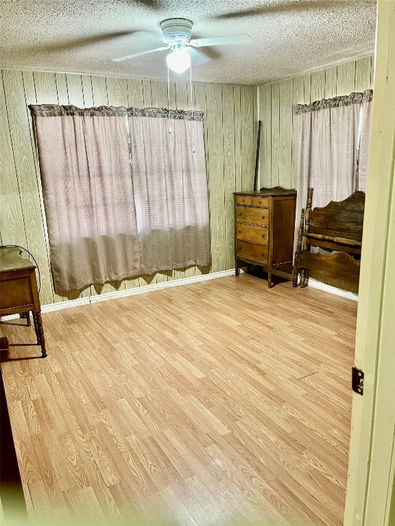 bedroom with a textured ceiling, wooden walls, light wood-type flooring, and ceiling fan