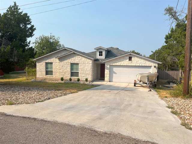 view of front of house with an attached garage, stone siding, fence, and concrete driveway