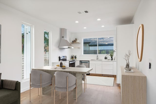 kitchen with sink, light hardwood / wood-style flooring, appliances with stainless steel finishes, a kitchen breakfast bar, and white cabinets