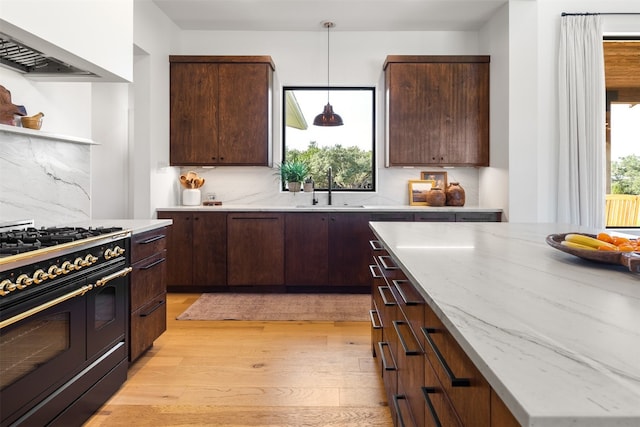 kitchen with pendant lighting, double oven range, backsplash, sink, and light wood-type flooring