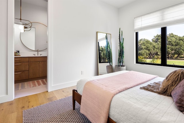 bedroom featuring light hardwood / wood-style floors, ensuite bath, and sink