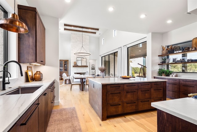 kitchen featuring light stone countertops, sink, light hardwood / wood-style flooring, beamed ceiling, and decorative light fixtures