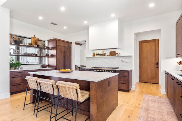 kitchen featuring a center island, tasteful backsplash, light hardwood / wood-style floors, a breakfast bar area, and stainless steel gas cooktop