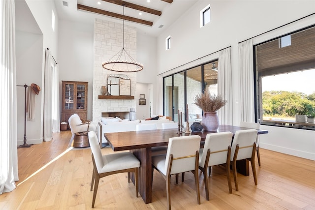 dining area featuring a fireplace, light hardwood / wood-style flooring, a notable chandelier, beamed ceiling, and a high ceiling