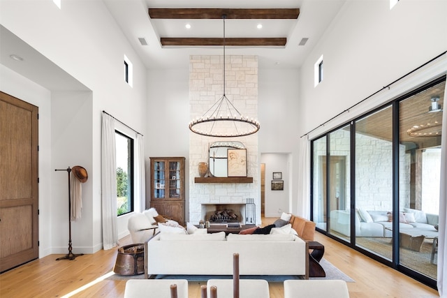 living room featuring a stone fireplace, light wood-type flooring, a towering ceiling, and an inviting chandelier