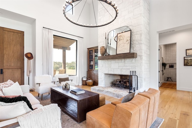 living room with a stone fireplace, light hardwood / wood-style flooring, and a towering ceiling