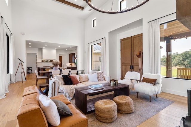 living room with beam ceiling, a towering ceiling, a chandelier, and light hardwood / wood-style floors