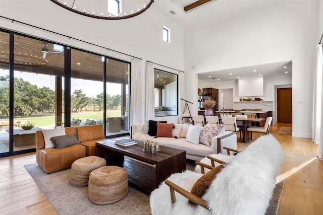 living room with a notable chandelier, plenty of natural light, a high ceiling, and light hardwood / wood-style flooring