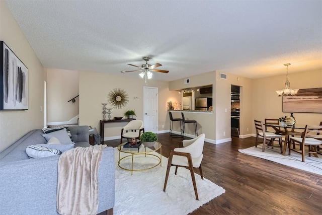 living room with ceiling fan with notable chandelier, a textured ceiling, and dark hardwood / wood-style flooring