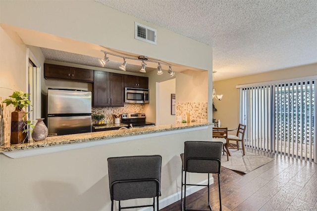 kitchen with kitchen peninsula, light stone countertops, appliances with stainless steel finishes, dark hardwood / wood-style flooring, and dark brown cabinetry