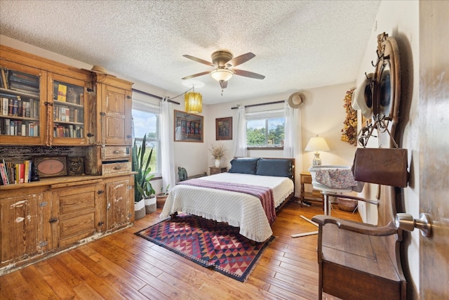 bedroom with a textured ceiling, wood-type flooring, and ceiling fan