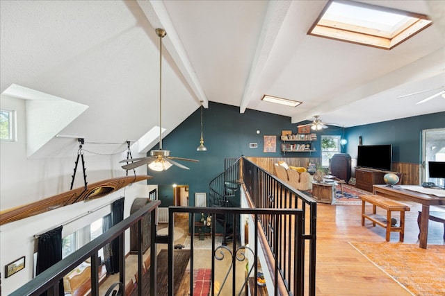 stairway with a wealth of natural light, lofted ceiling with skylight, wooden walls, and hardwood / wood-style flooring